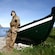 A fisherman dressed in handmade clothes and moccasins leans against a rowboat